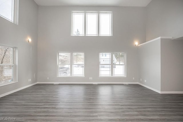 unfurnished living room with dark wood-type flooring, a towering ceiling, and plenty of natural light