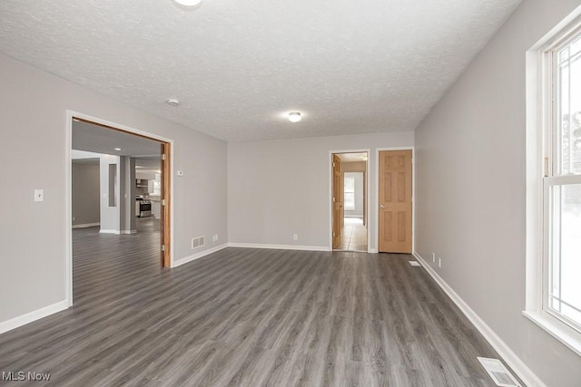 spare room featuring a healthy amount of sunlight, a textured ceiling, and dark hardwood / wood-style flooring