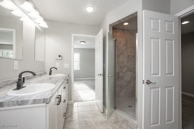 bathroom with a textured ceiling, vanity, a tile shower, and tile patterned flooring