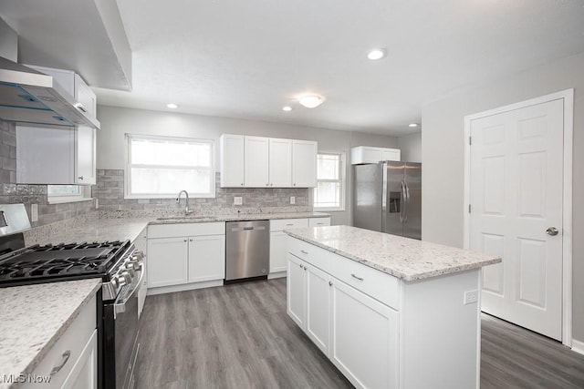 kitchen with appliances with stainless steel finishes, white cabinetry, sink, a kitchen island, and light stone counters