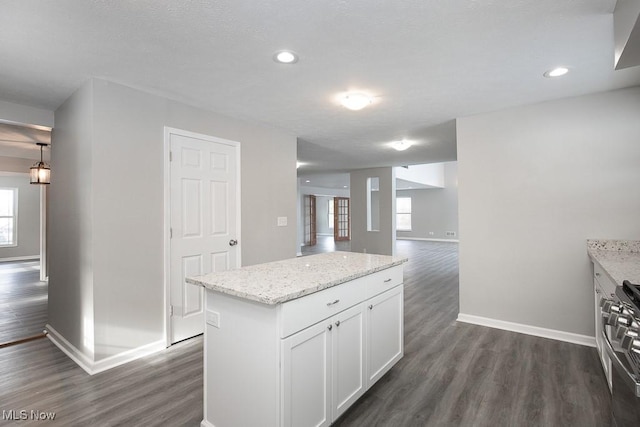 kitchen with pendant lighting, dark hardwood / wood-style flooring, white cabinets, light stone counters, and a center island