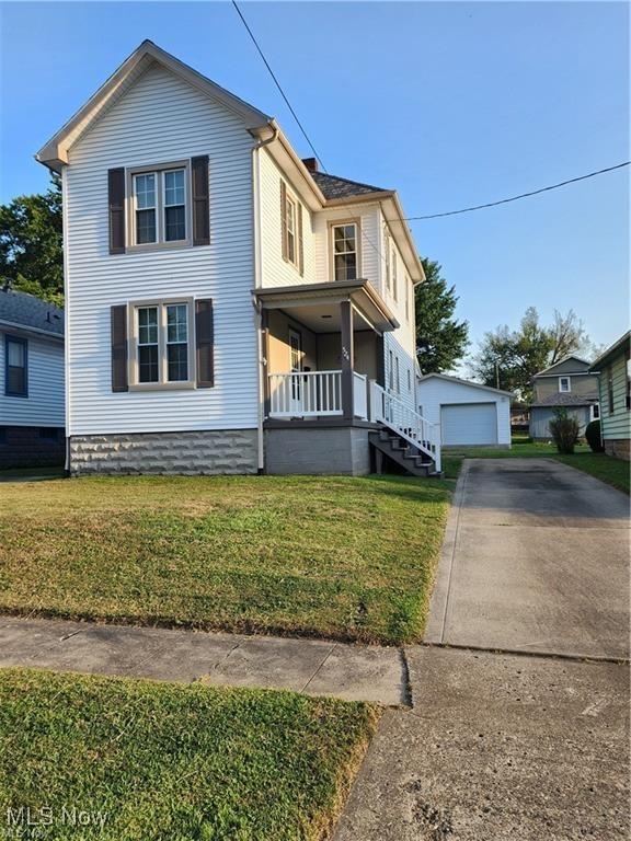 view of front of home with covered porch, an outbuilding, a garage, and a front lawn