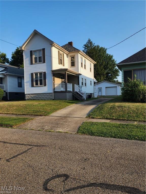 view of front of house featuring covered porch, a front yard, a garage, and an outdoor structure