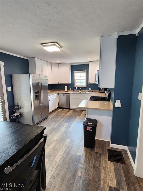 kitchen featuring a textured ceiling, white cabinets, appliances with stainless steel finishes, kitchen peninsula, and hardwood / wood-style flooring