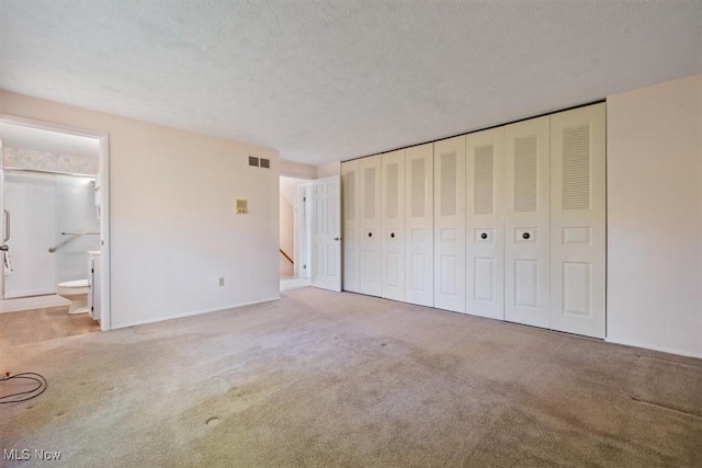 unfurnished bedroom with a textured ceiling, ensuite bath, and carpet floors