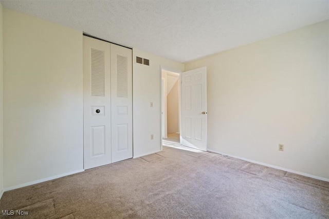 unfurnished bedroom with light carpet, a textured ceiling, and a closet