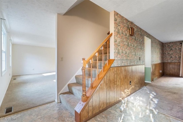 stairs with a textured ceiling, wood walls, and carpet flooring