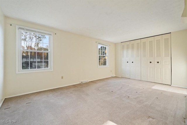 unfurnished bedroom featuring a closet, light carpet, and multiple windows