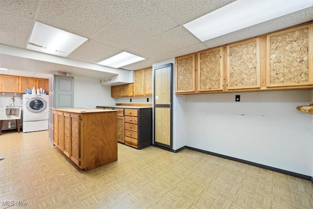 kitchen featuring sink, washer / clothes dryer, a paneled ceiling, a kitchen island, and light parquet floors