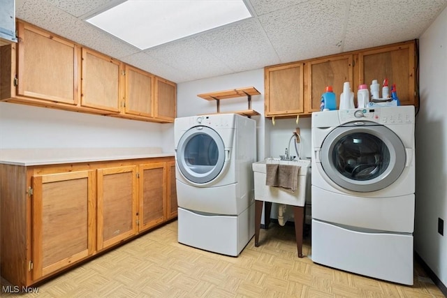 laundry area featuring sink, cabinets, light parquet floors, and washing machine and clothes dryer