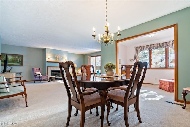 dining area featuring light carpet, a tile fireplace, and an inviting chandelier