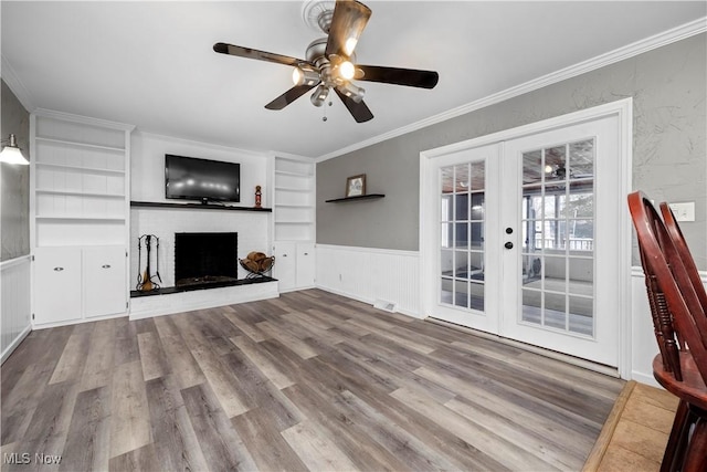 unfurnished living room featuring crown molding, french doors, built in features, light wood-type flooring, and a brick fireplace