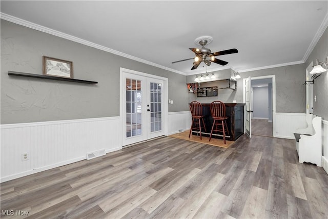 unfurnished living room with hardwood / wood-style flooring, bar area, crown molding, and french doors