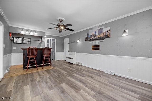 dining space with ceiling fan, wood-type flooring, ornamental molding, and indoor bar