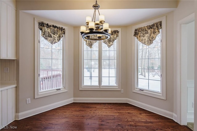 unfurnished dining area featuring a chandelier, a wealth of natural light, and dark hardwood / wood-style flooring