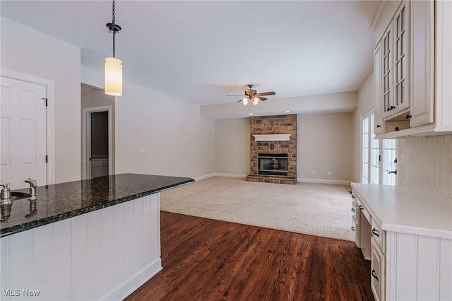 kitchen with pendant lighting, ceiling fan, dark hardwood / wood-style flooring, white cabinetry, and a stone fireplace