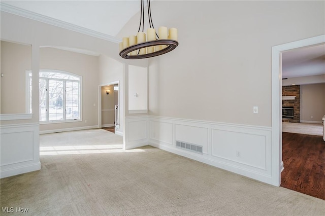 carpeted empty room with vaulted ceiling, a chandelier, a brick fireplace, and crown molding