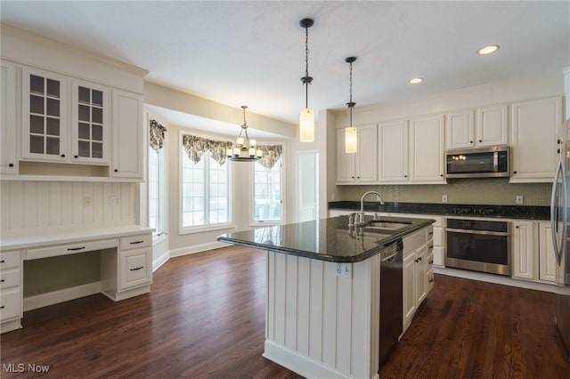 kitchen with sink, built in desk, white cabinets, stainless steel appliances, and a center island with sink