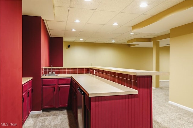 kitchen with a paneled ceiling, light carpet, sink, kitchen peninsula, and a breakfast bar area