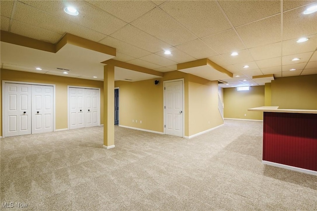 basement featuring a drop ceiling, light colored carpet, and bar area