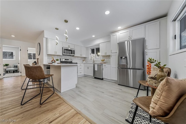 kitchen with appliances with stainless steel finishes, white cabinetry, a breakfast bar area, hanging light fixtures, and light wood-type flooring