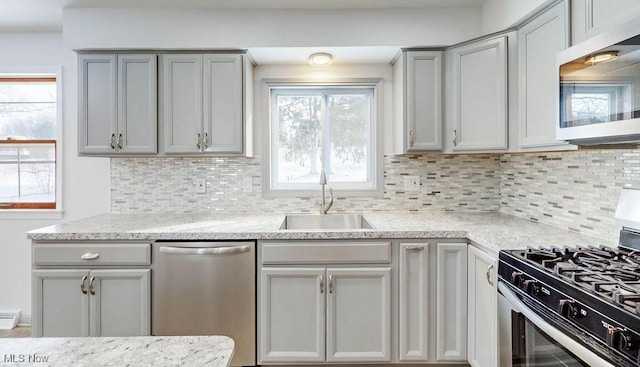 kitchen featuring light stone countertops, appliances with stainless steel finishes, sink, backsplash, and gray cabinets