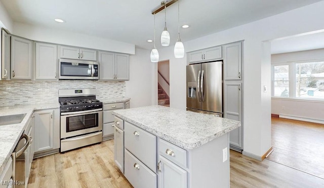 kitchen with a baseboard radiator, appliances with stainless steel finishes, tasteful backsplash, gray cabinets, and a center island