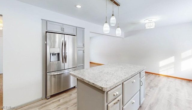 kitchen with a center island, stainless steel refrigerator with ice dispenser, hanging light fixtures, gray cabinets, and light wood-type flooring