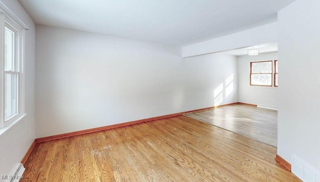 spare room featuring a baseboard radiator, light wood-type flooring, and plenty of natural light