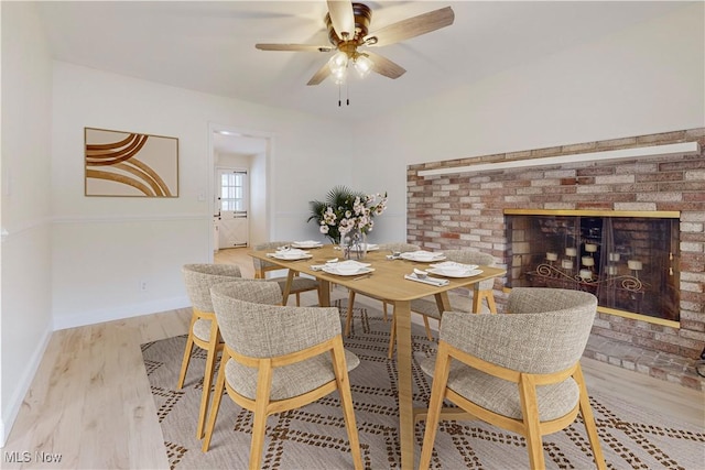 dining space with a brick fireplace, light hardwood / wood-style flooring, and ceiling fan