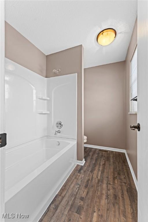 bathroom featuring washtub / shower combination, hardwood / wood-style floors, and toilet