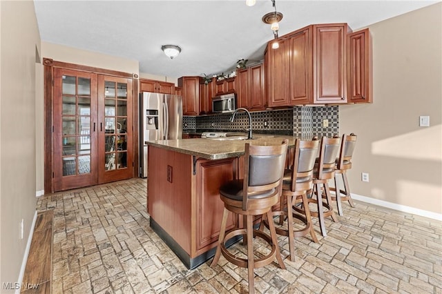 kitchen with a kitchen bar, stainless steel appliances, french doors, tasteful backsplash, and kitchen peninsula