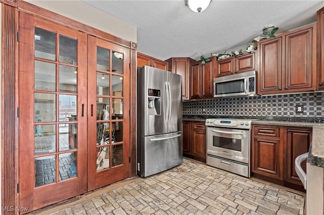 kitchen featuring appliances with stainless steel finishes, a textured ceiling, tasteful backsplash, dark stone countertops, and french doors