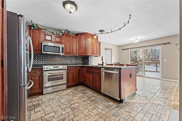 kitchen with appliances with stainless steel finishes, a textured ceiling, decorative backsplash, sink, and kitchen peninsula