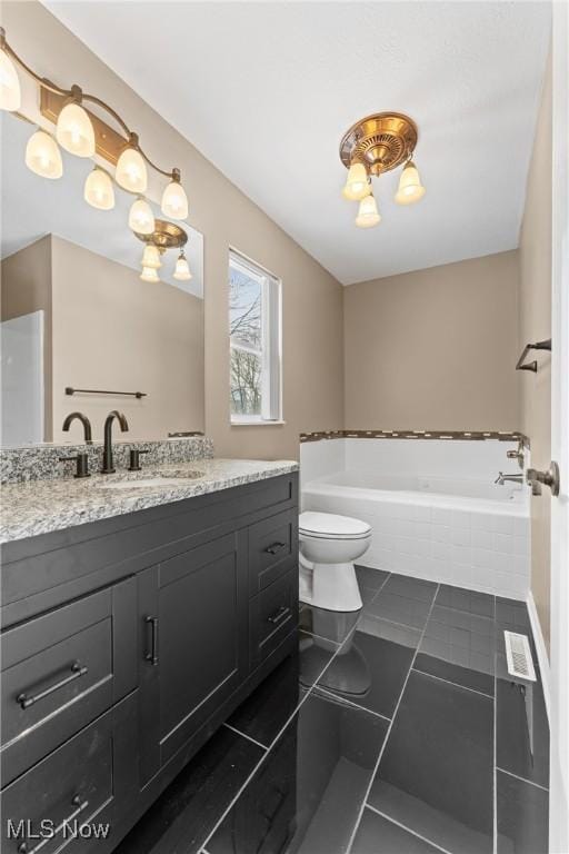 bathroom featuring tiled bath, toilet, vanity, and tile patterned flooring