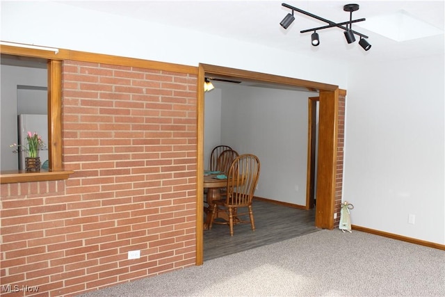 carpeted dining room with brick wall and baseboards