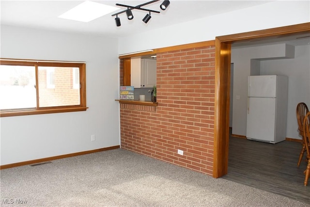 unfurnished living room featuring dark carpet, brick wall, and a skylight