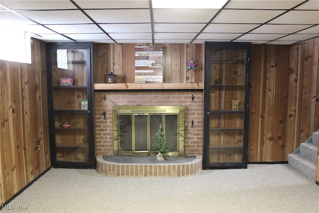 carpeted living room featuring a fireplace, wooden walls, and stairs