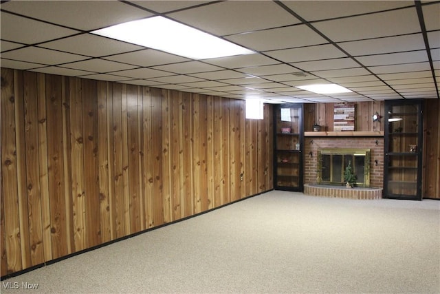 basement featuring a paneled ceiling, carpet flooring, wood walls, and a fireplace