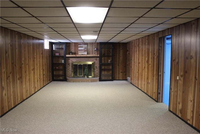 basement featuring wooden walls, a paneled ceiling, carpet floors, and a brick fireplace