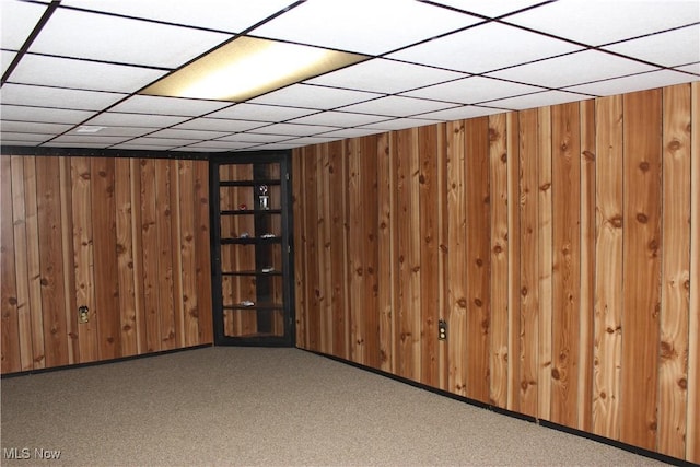 basement featuring a drop ceiling, light carpet, and wooden walls