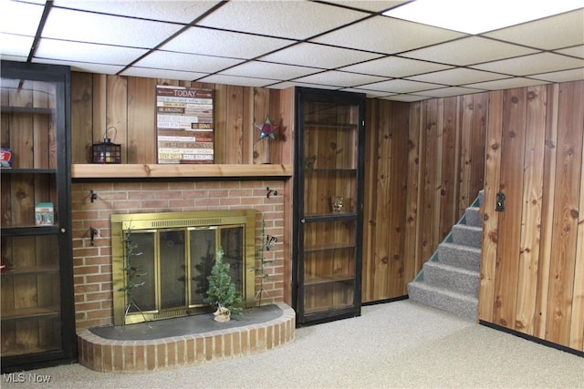 unfurnished living room with a brick fireplace, stairway, carpet, and wooden walls