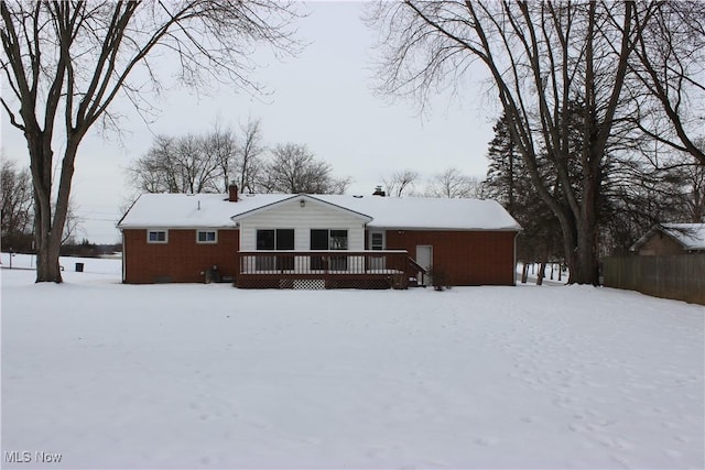 snow covered back of property featuring brick siding and a wooden deck