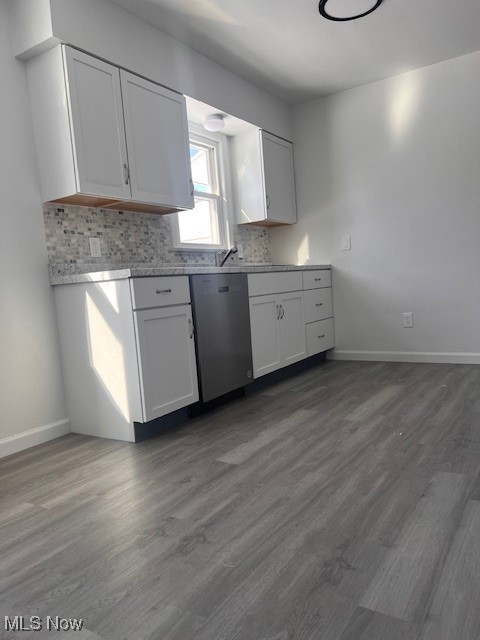 kitchen with stainless steel dishwasher, white cabinets, dark wood-type flooring, light stone countertops, and decorative backsplash