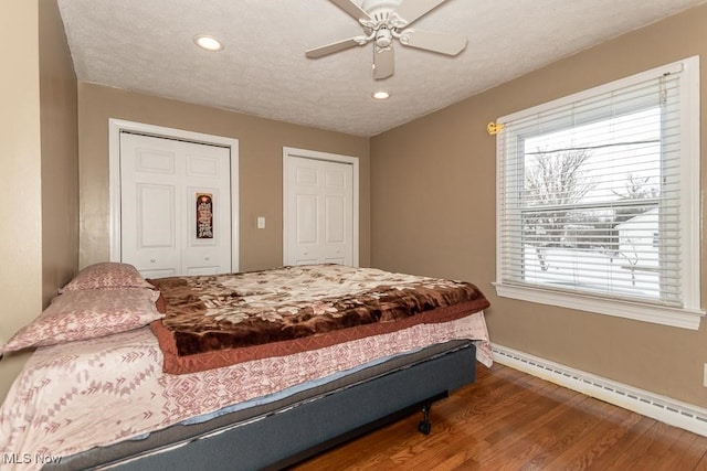 bedroom featuring ceiling fan, a baseboard radiator, multiple windows, and hardwood / wood-style flooring