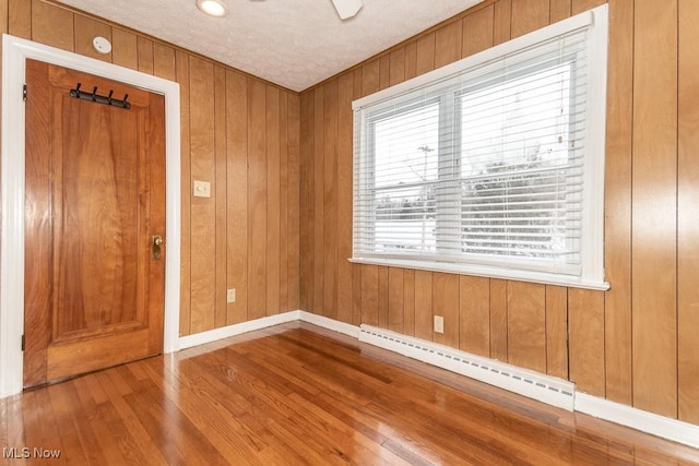 spare room with wood-type flooring, wood walls, a textured ceiling, and a baseboard heating unit