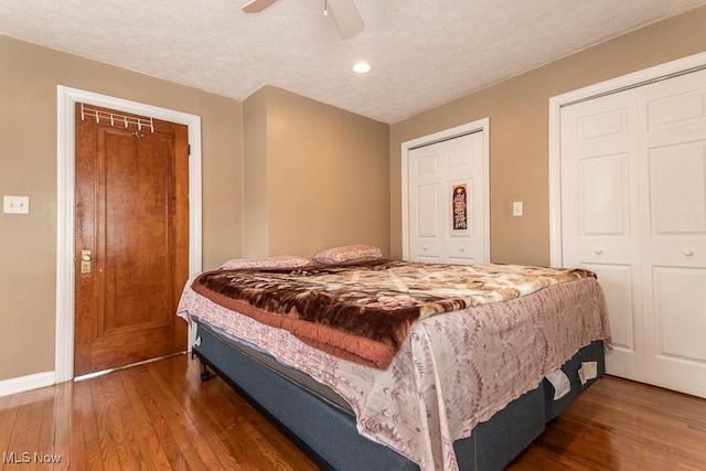 bedroom with ceiling fan, dark hardwood / wood-style floors, a textured ceiling, and two closets