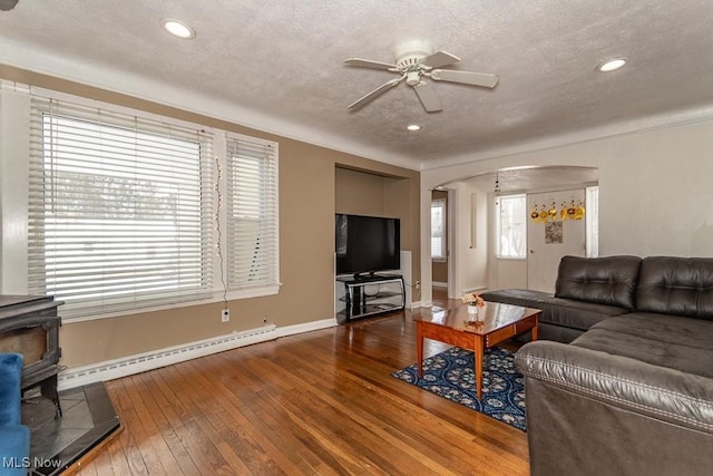 living room featuring a wood stove, baseboard heating, a textured ceiling, and hardwood / wood-style flooring