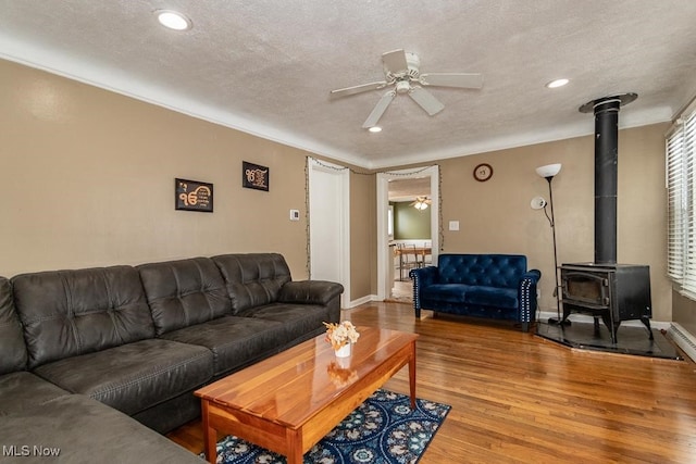 living room with ceiling fan, a wood stove, wood-type flooring, and a textured ceiling