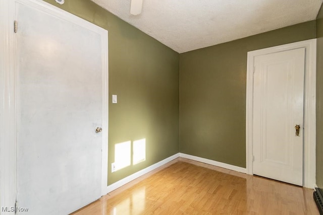 spare room featuring light hardwood / wood-style floors, baseboard heating, and a textured ceiling